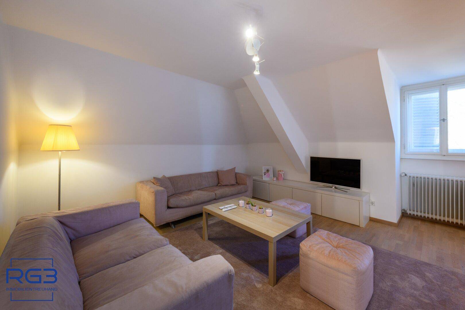 Gemütlicher Wohnbereich im Dachgeschoss mit schrägen Wänden, Sofa und Teppichboden.