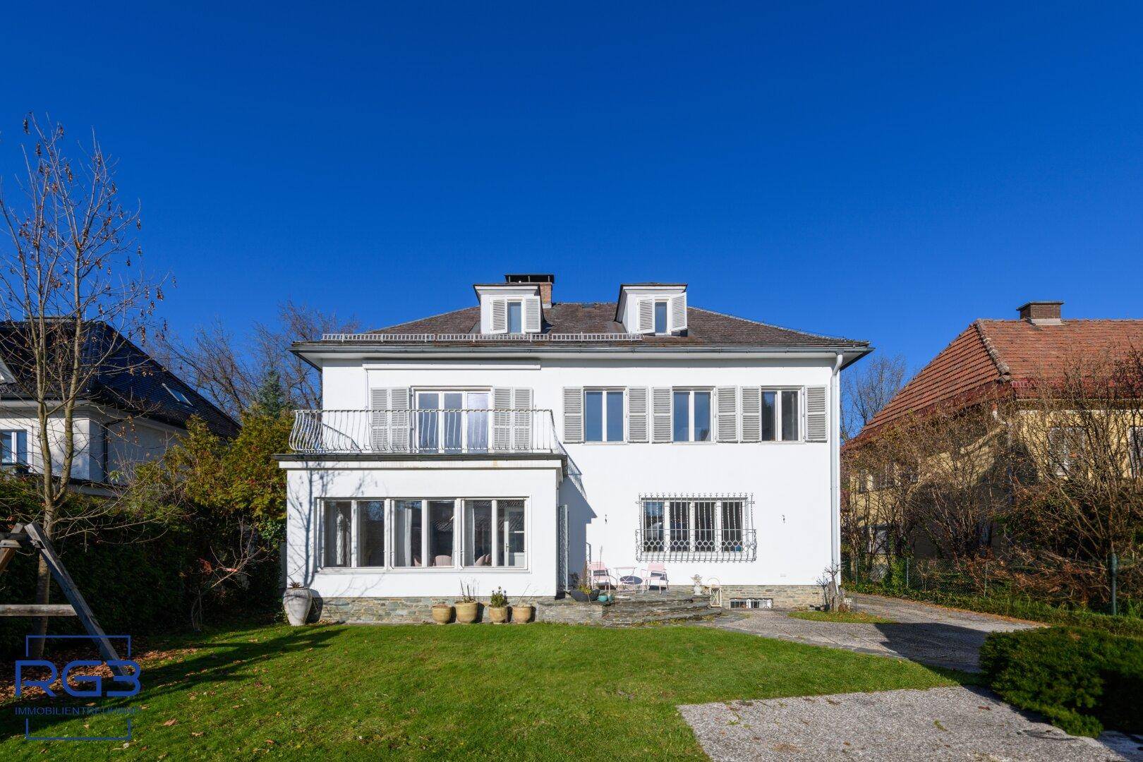 Elegantes weißes Haus mit Balkon, großen Fenstern und gepflegtem Vorgarten.
