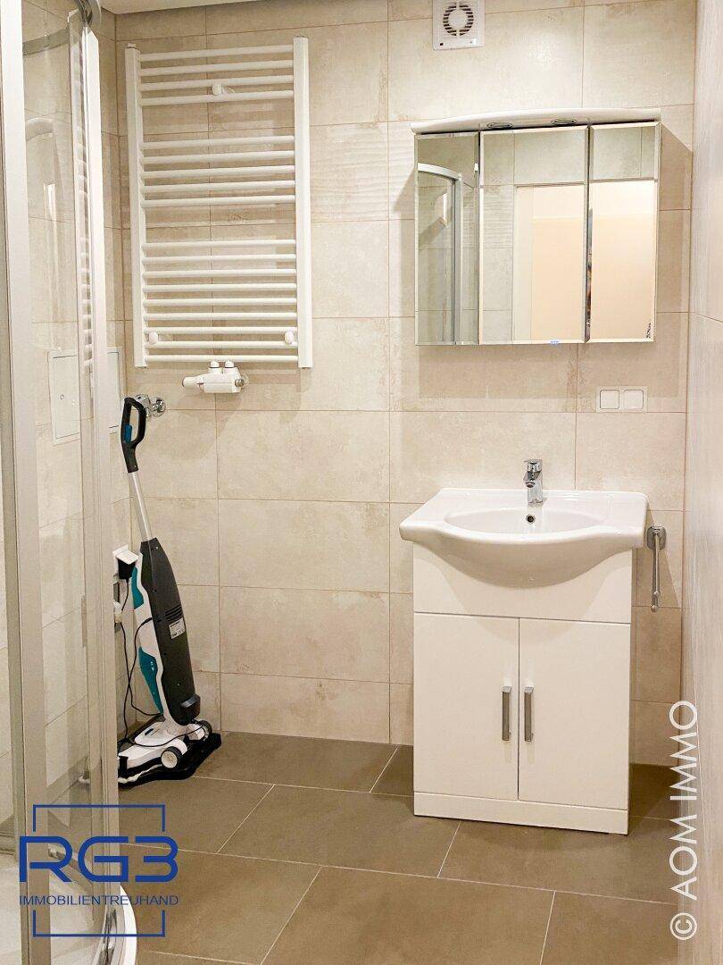 Badezimmer mit beigefarbenen Fliesen, Duschkabine, Waschtisch und beheiztem Handtuchhalter.