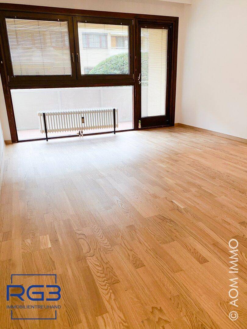 Heller Wohnraum mit Eichenparkett und großen Fenstern mit Jalousien, die viel Tageslicht hereinlassen.
