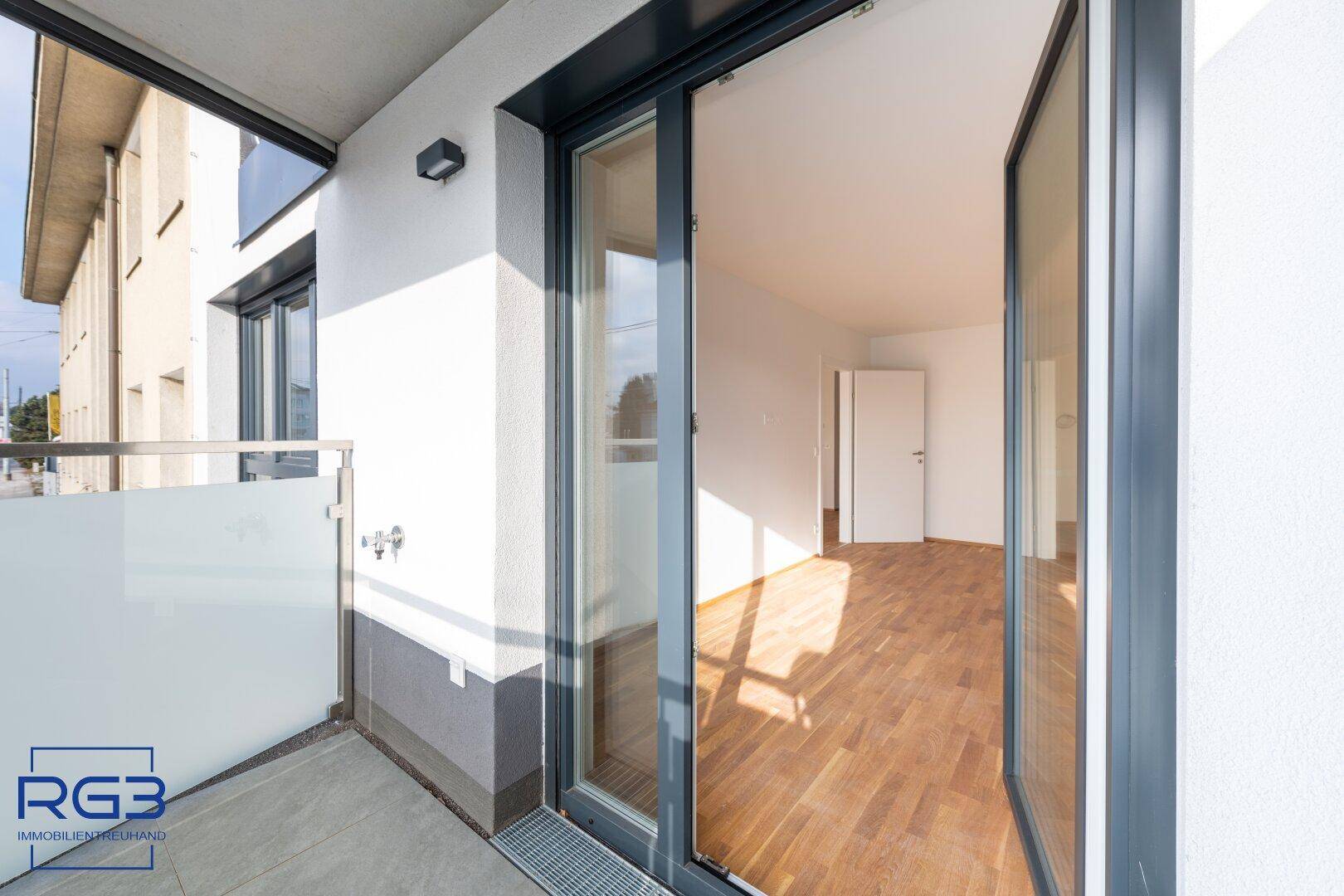 Moderner Balkon mit Glasbrüstung und Zugang zu einem hellen Innenraum.