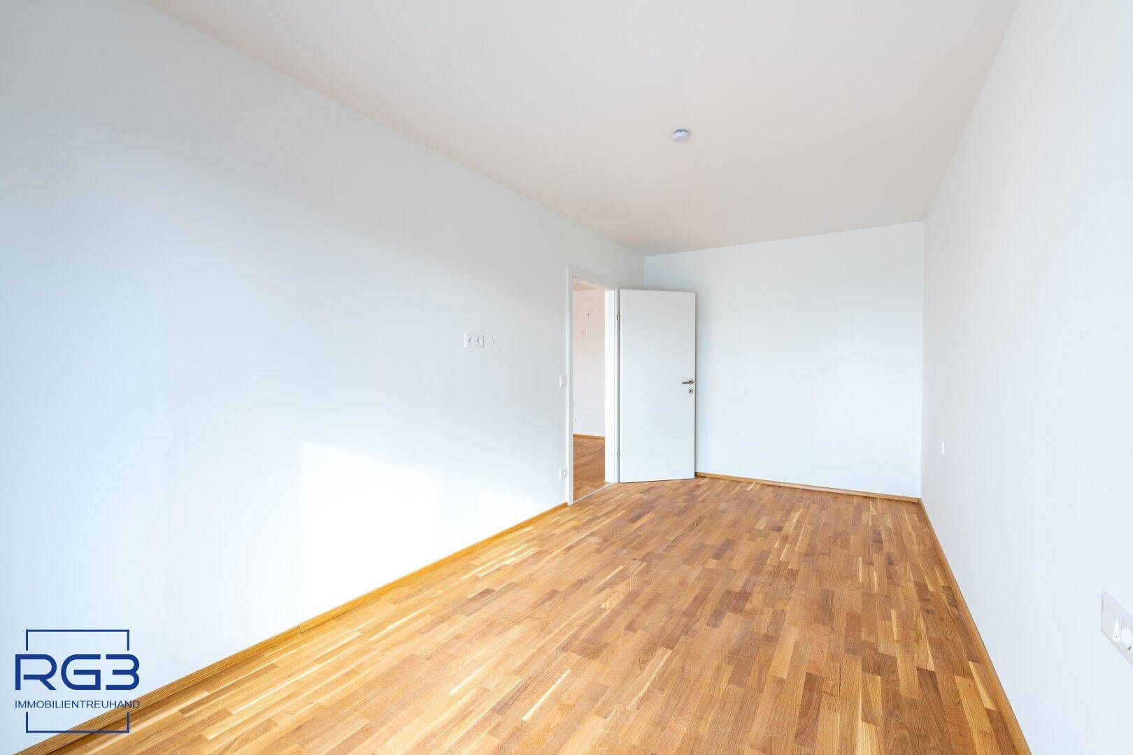 Leeres Zimmer mit Parkettboden und weiß gestrichenen Wänden, bereit zur Einrichtung.