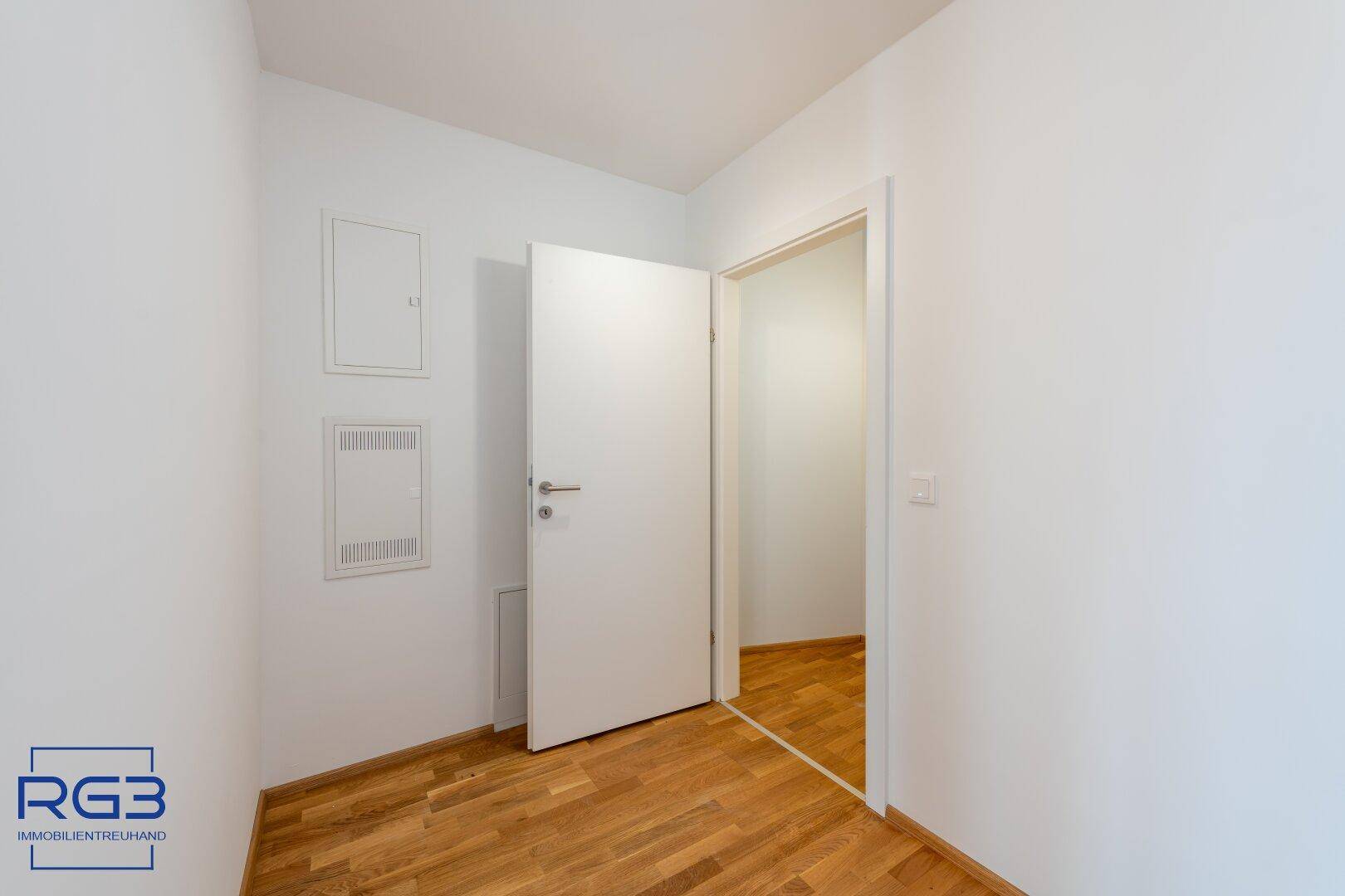 Heller Flur mit Parkettboden und weißer Tür, der zu einem weiteren Raum führt.