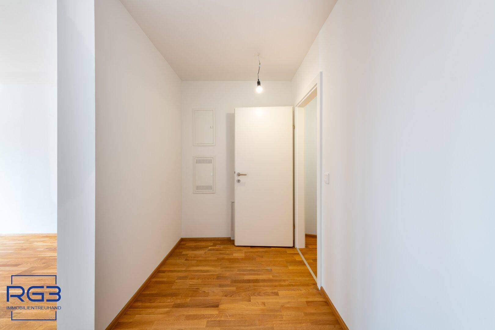 Schlichter Flur mit Parkettboden und weiß gestrichenen Wänden, bietet Zugang zu mehreren Zimmern.