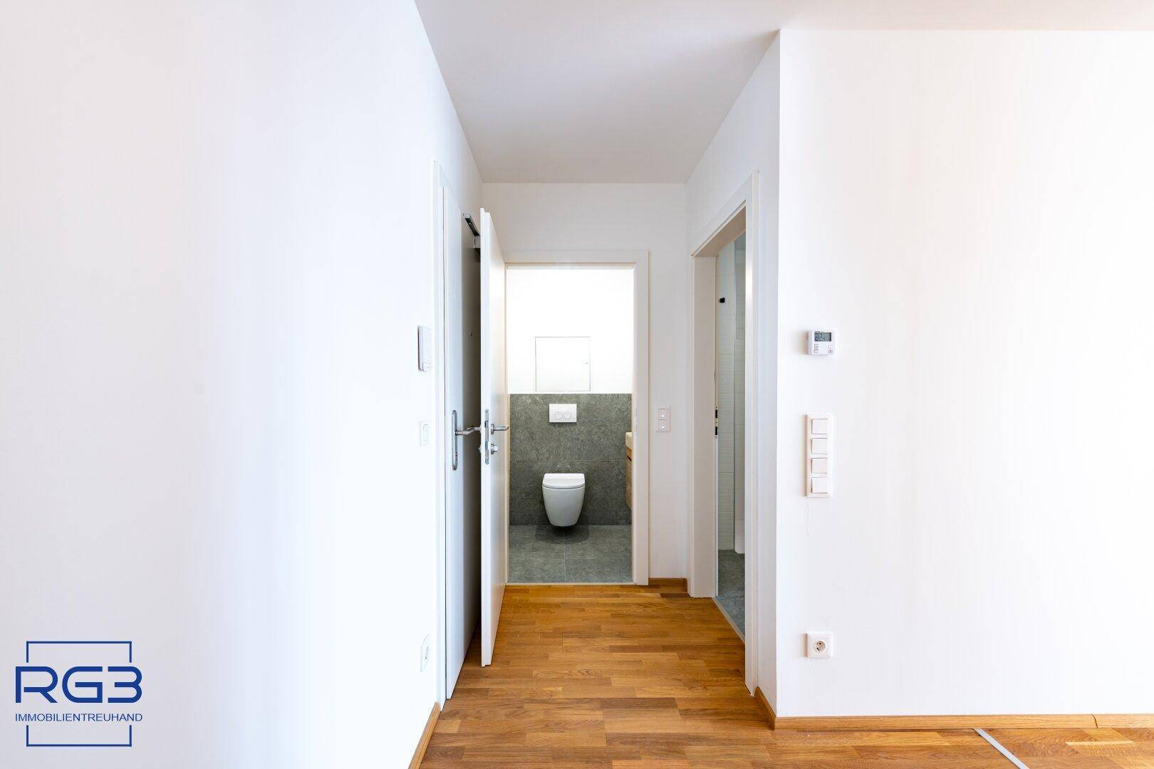 Flur mit Blick auf ein separates WC mit Wand-WC und modernen Fliesen.