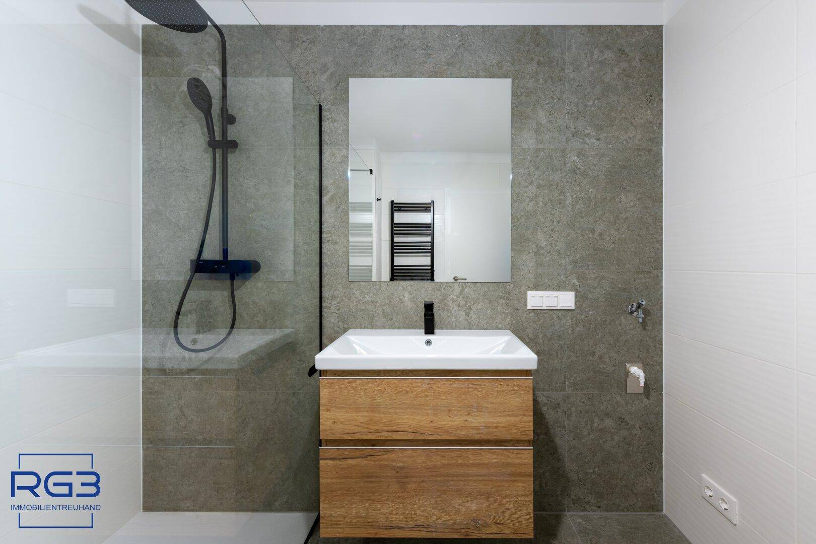 Elegantes Badezimmer mit moderner Duschkabine, Holzwaschtisch und dunklen Armaturen.