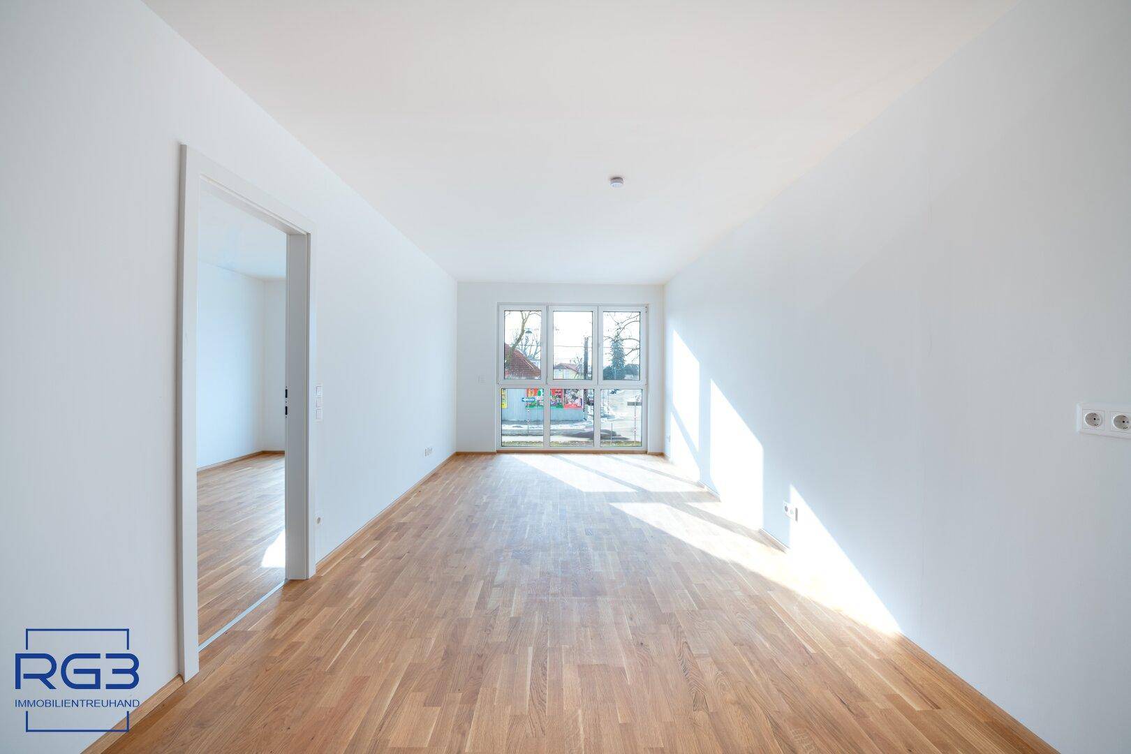 Lichtdurchflutetes Wohnzimmer mit hellem Parkettboden und viel Tageslicht durch große Fenster.