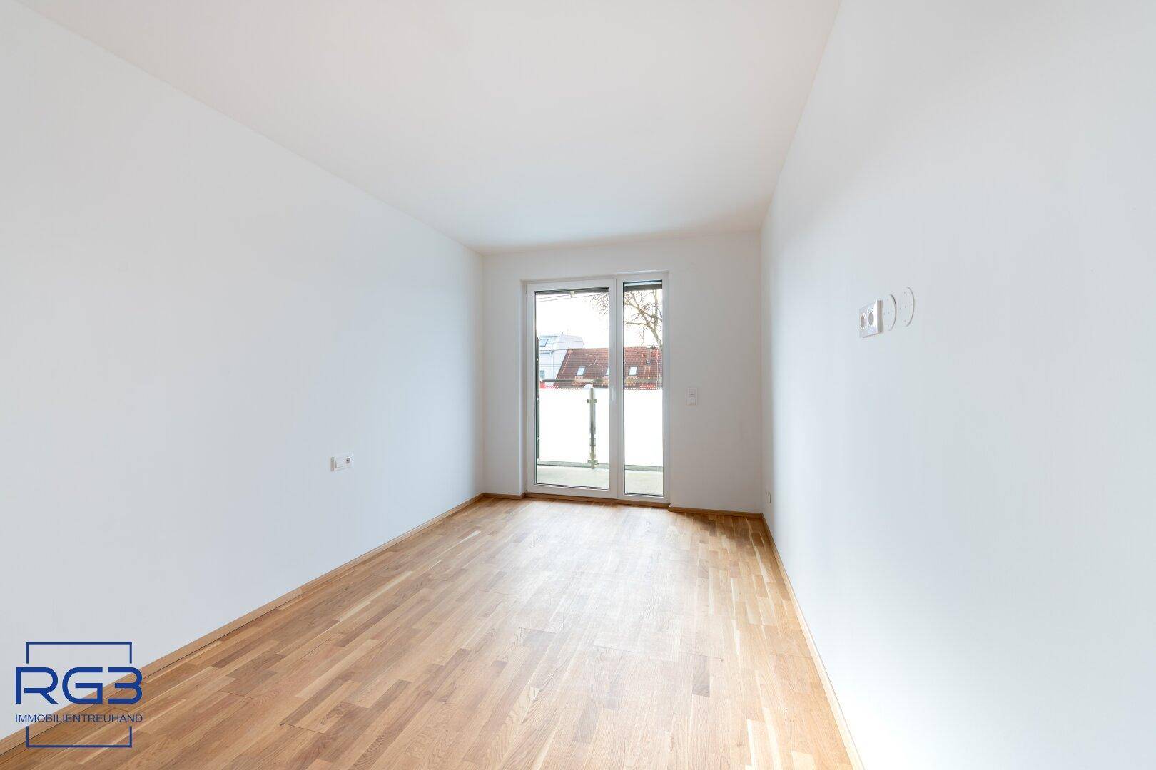 Helles Schlafzimmer mit Parkettboden und Zugang zu einem französischen Balkon.