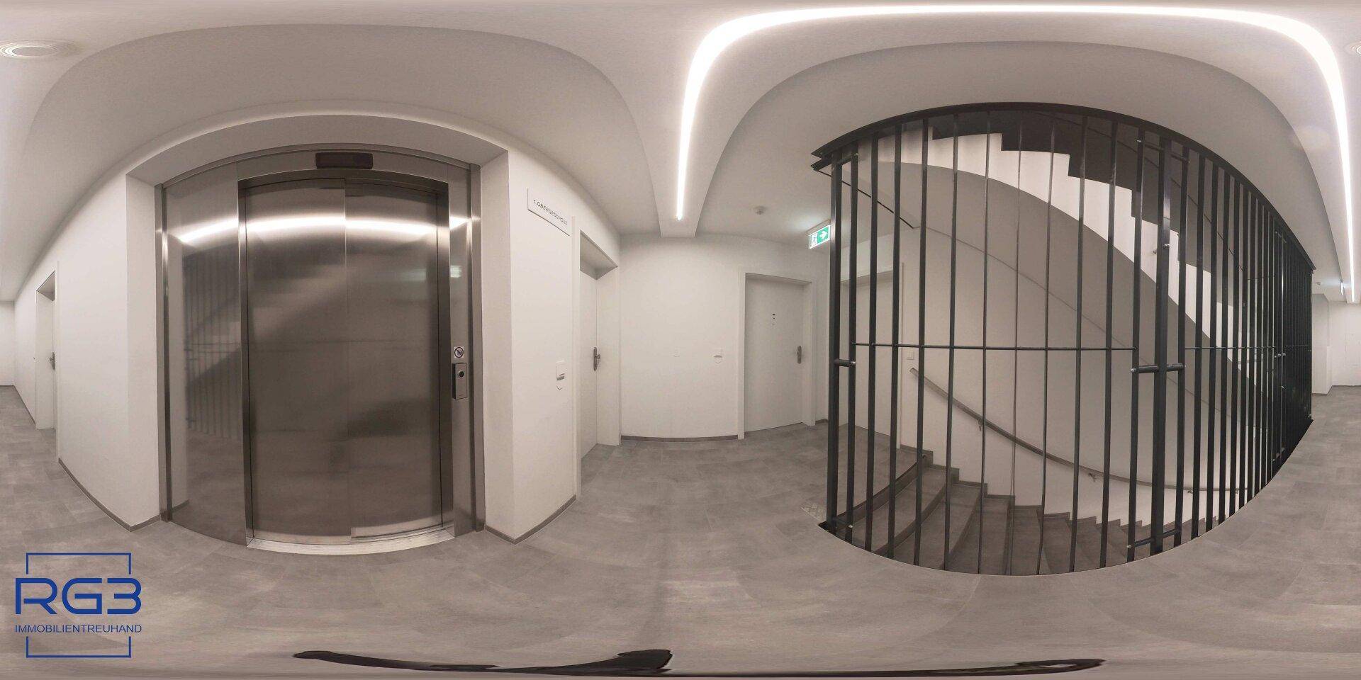 Moderner Eingangsbereich mit Aufzug, Treppenhaus und indirekter Deckenbeleuchtung.
