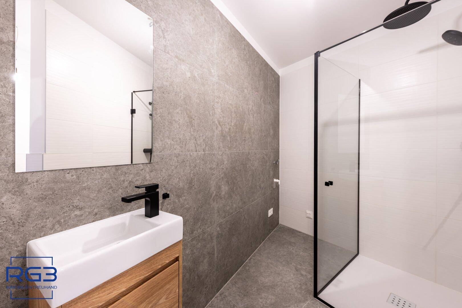 Modernes Badezimmer mit begehbarer Dusche, eleganten schwarzen Armaturen und Holzwaschtisch.