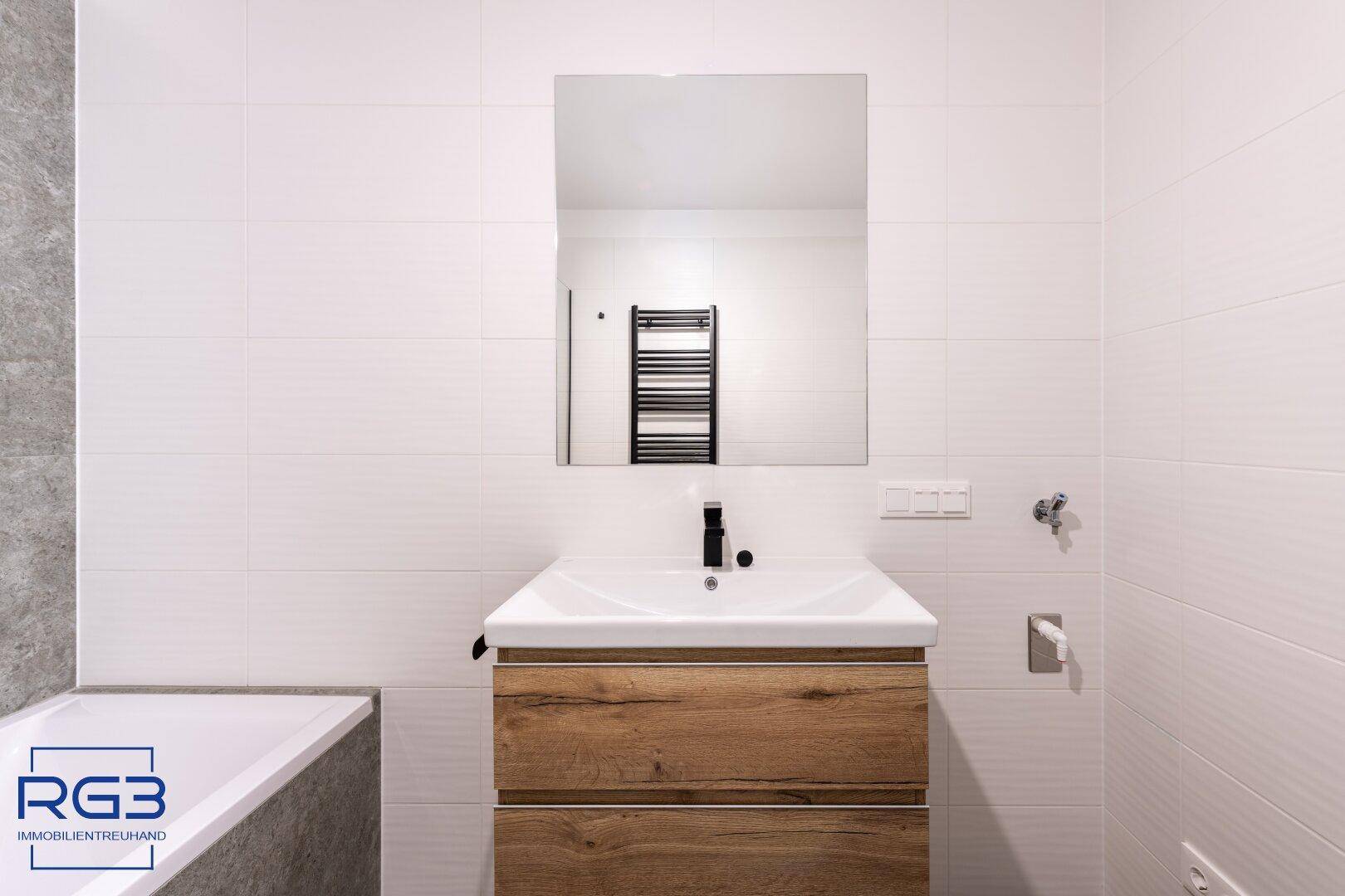 Detailansicht des modernen Waschbeckens mit Holzunterschrank und großem Spiegel im Badezimmer.