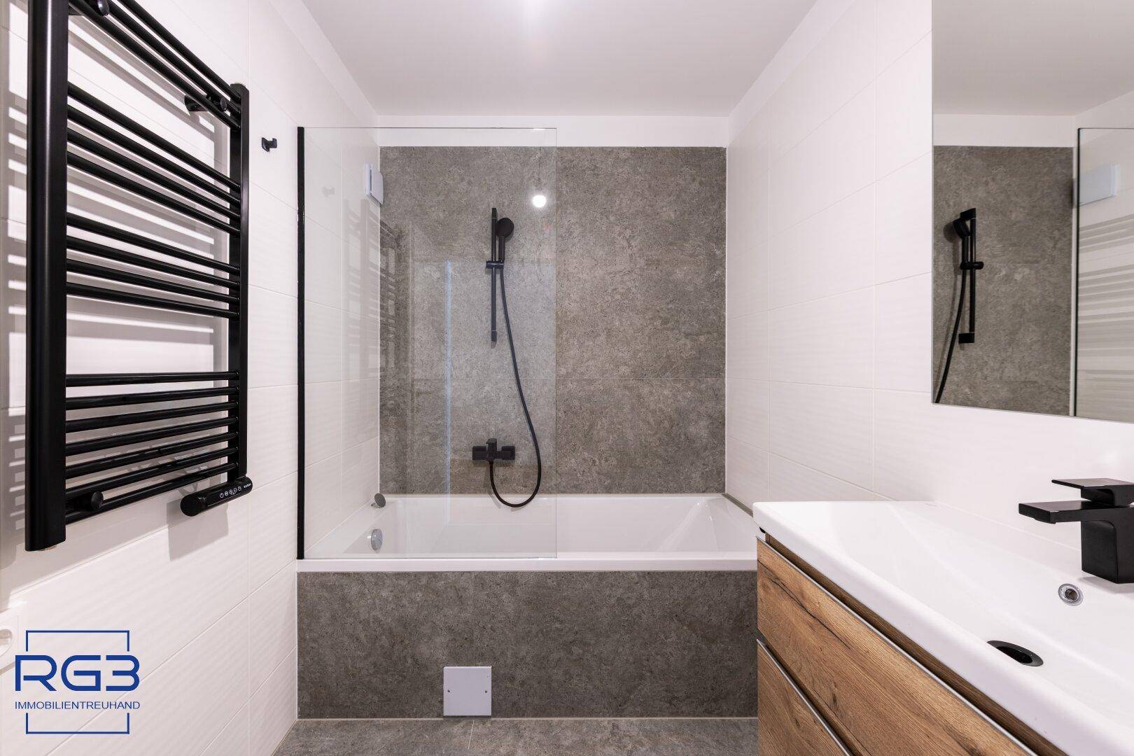 Stilvolles Badezimmer mit Badewanne, schwarzem Handtuchheizkörper und modernem Waschtisch.