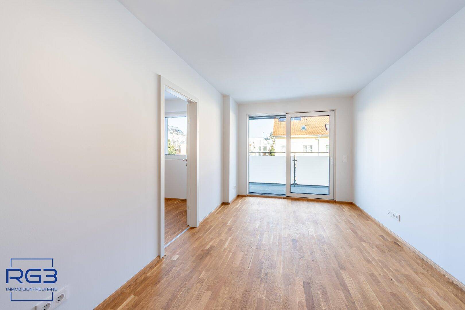 Geräumiges, helles Zimmer mit Holzboden und Schiebetür zum Balkon, bietet viel Tageslicht.