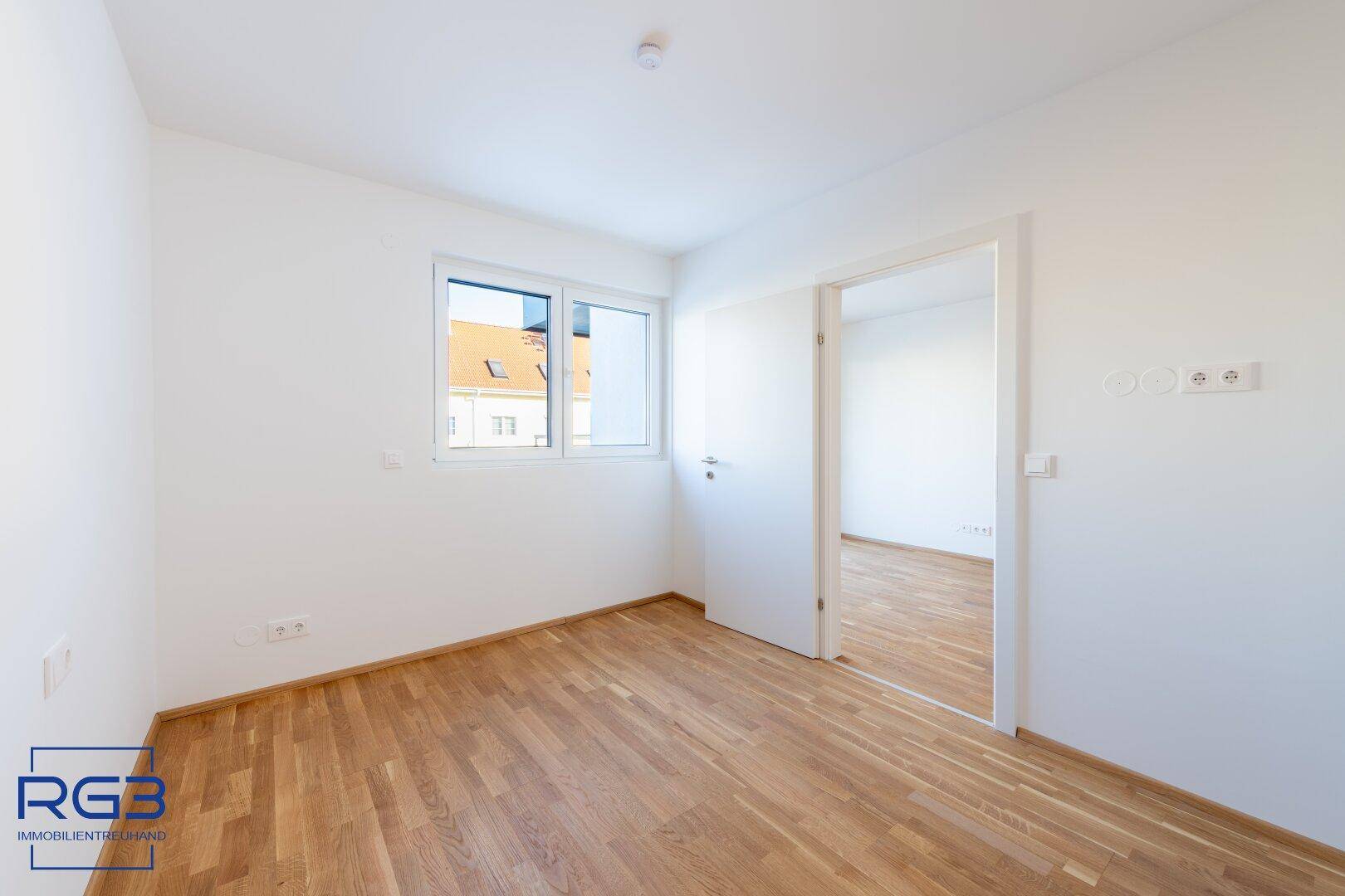 Lichtdurchflutetes Schlafzimmer mit Parkettboden und Fenster, bietet einen ruhigen Rückzugsort.