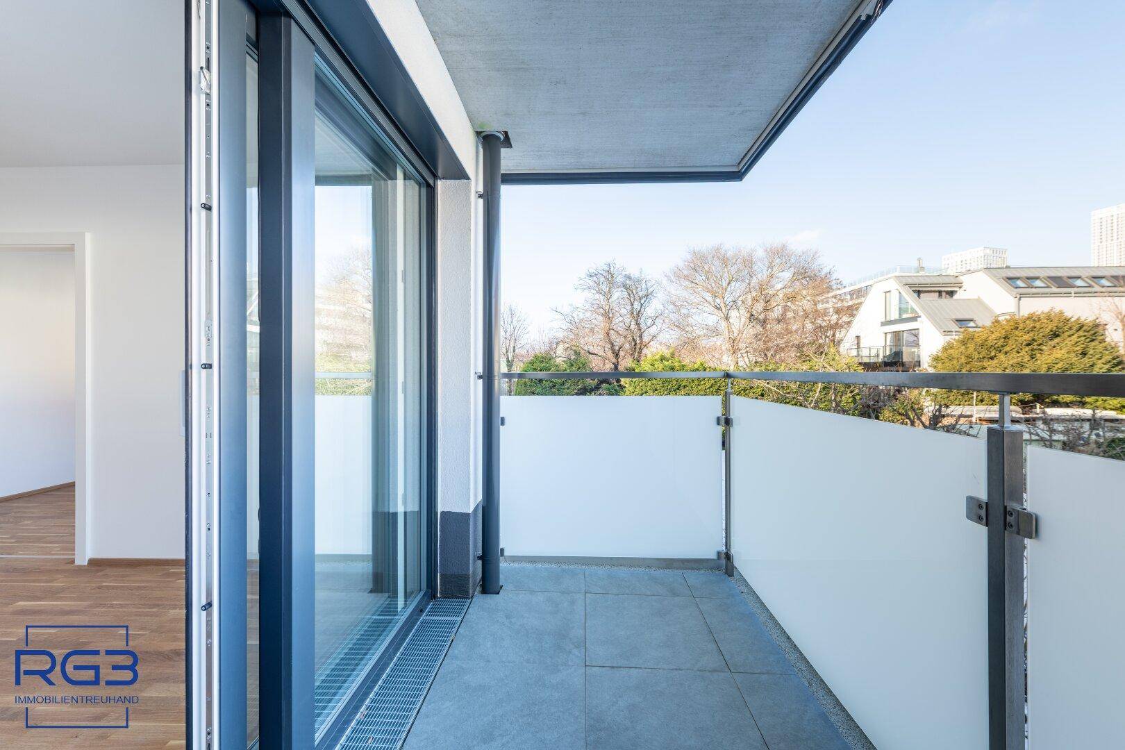 Moderner Balkon mit Fliesenboden und Glasgeländer, bietet einen Blick auf die Umgebung.