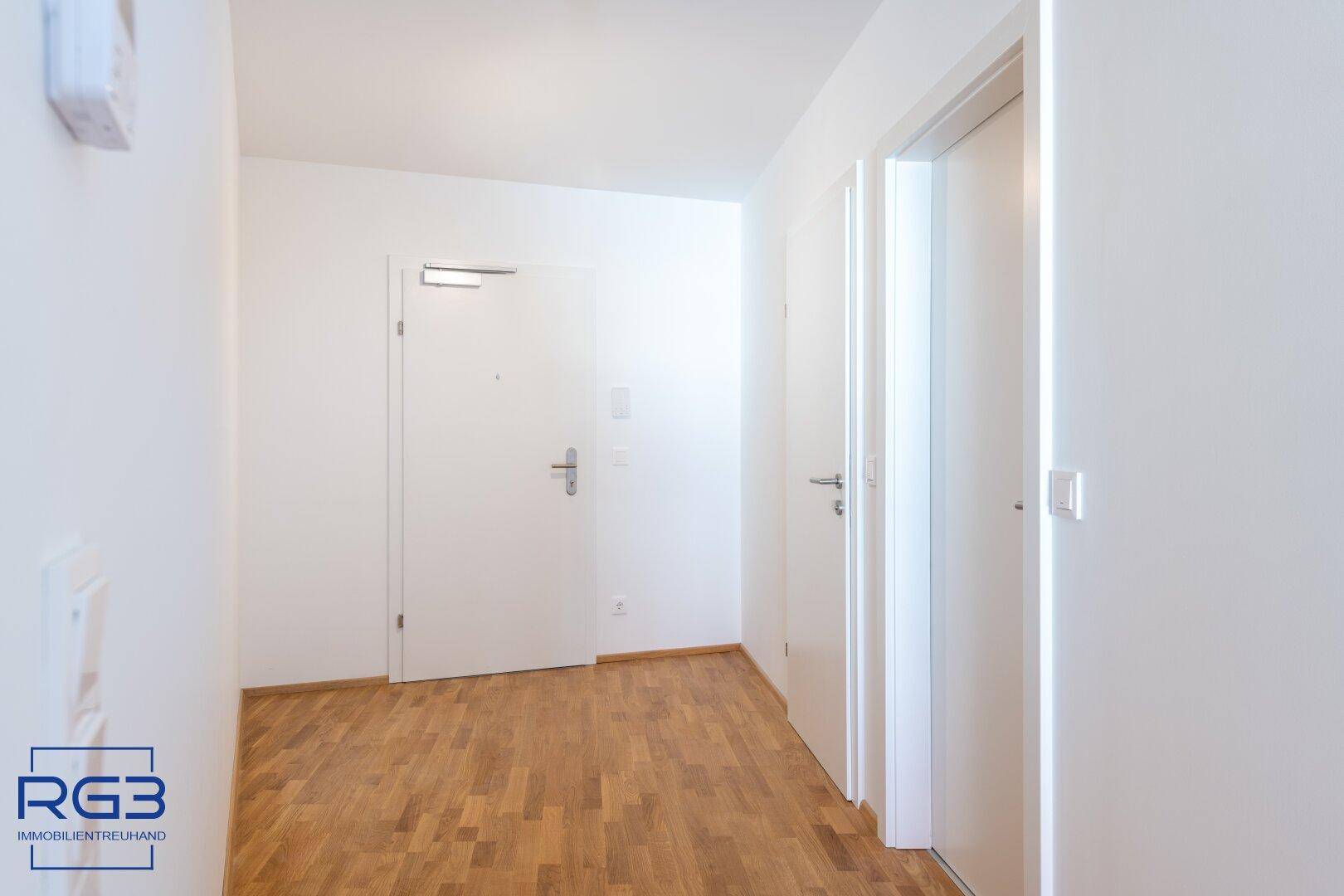 Heller Eingangsbereich mit Parkettboden und weißer Eingangstür, empfängt Bewohner und Gäste.