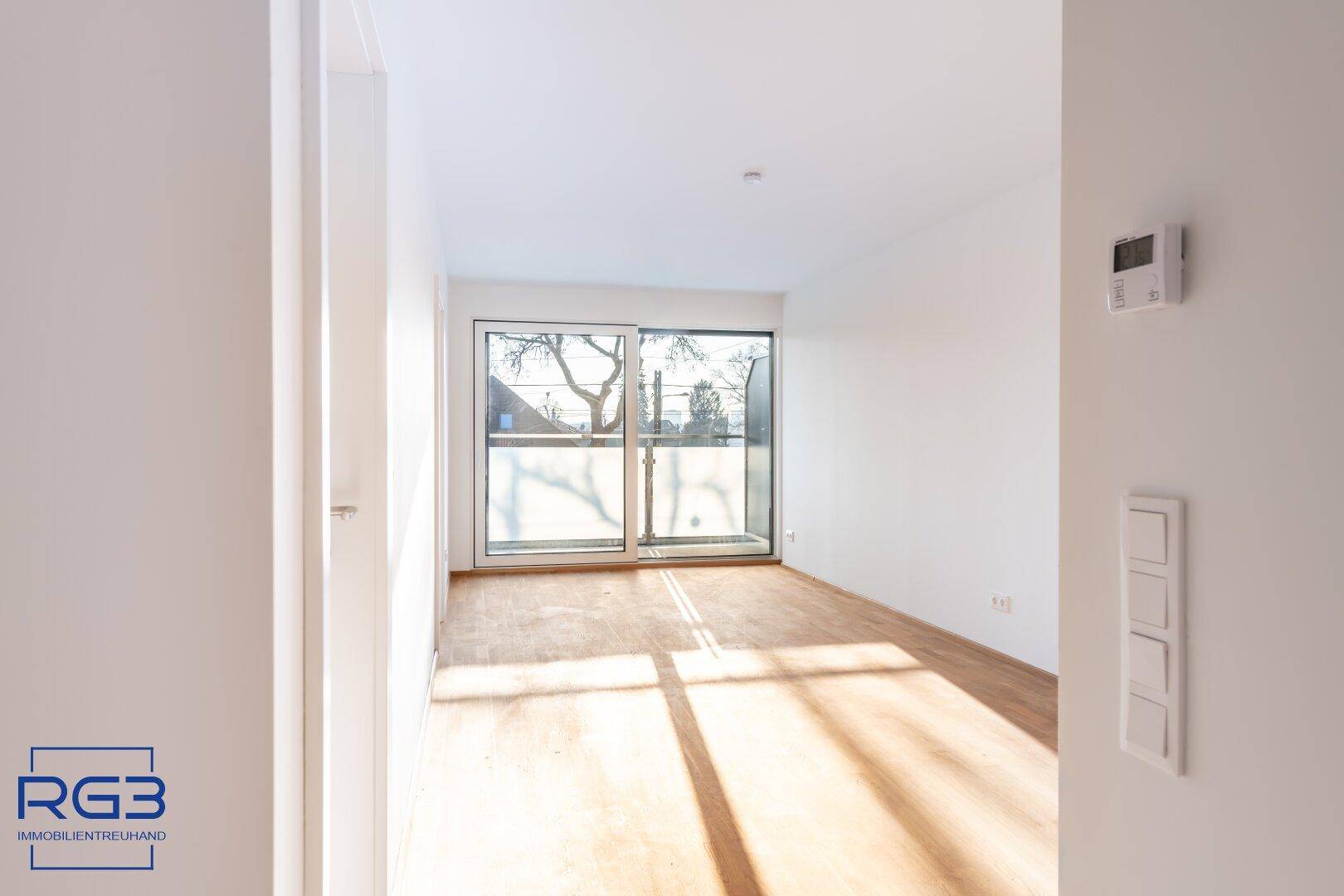 Sonniger Raum mit Holzboden und Balkonzugang, ausgestattet mit einem Thermostat an der Wand.