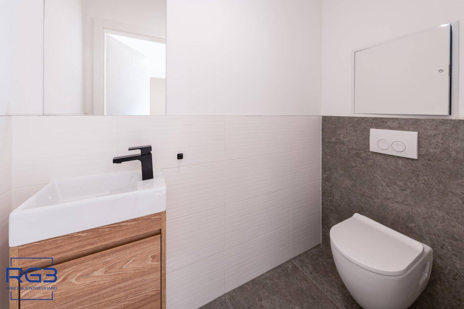 Modernes Gäste-WC mit wandhängender Toilette und kleinem Waschtisch, in Grau und Weiß gehalten.