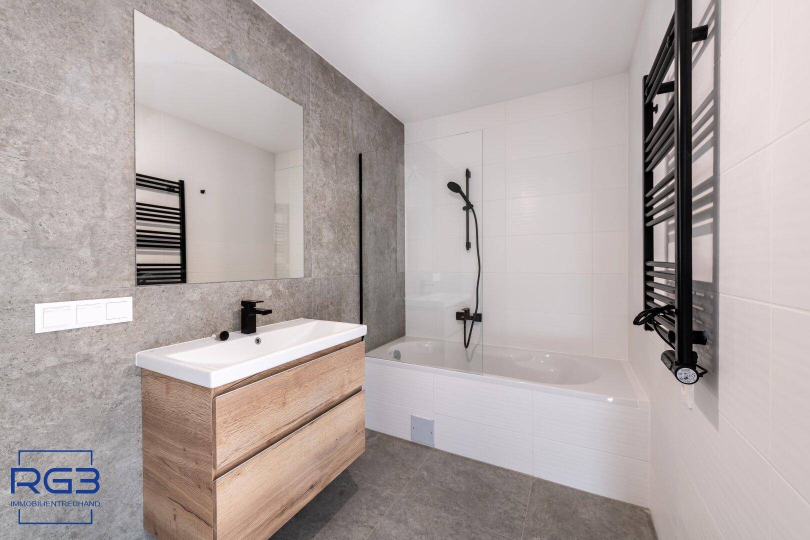 Modernes Badezimmer mit Badewanne, Holzwaschtisch und dunklen Armaturen, elegant gefliest.
