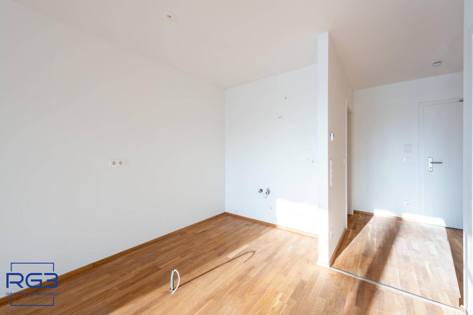 Heller Raum mit Holzboden und Anschlüssen, der auf die Installation einer Küche wartet.
