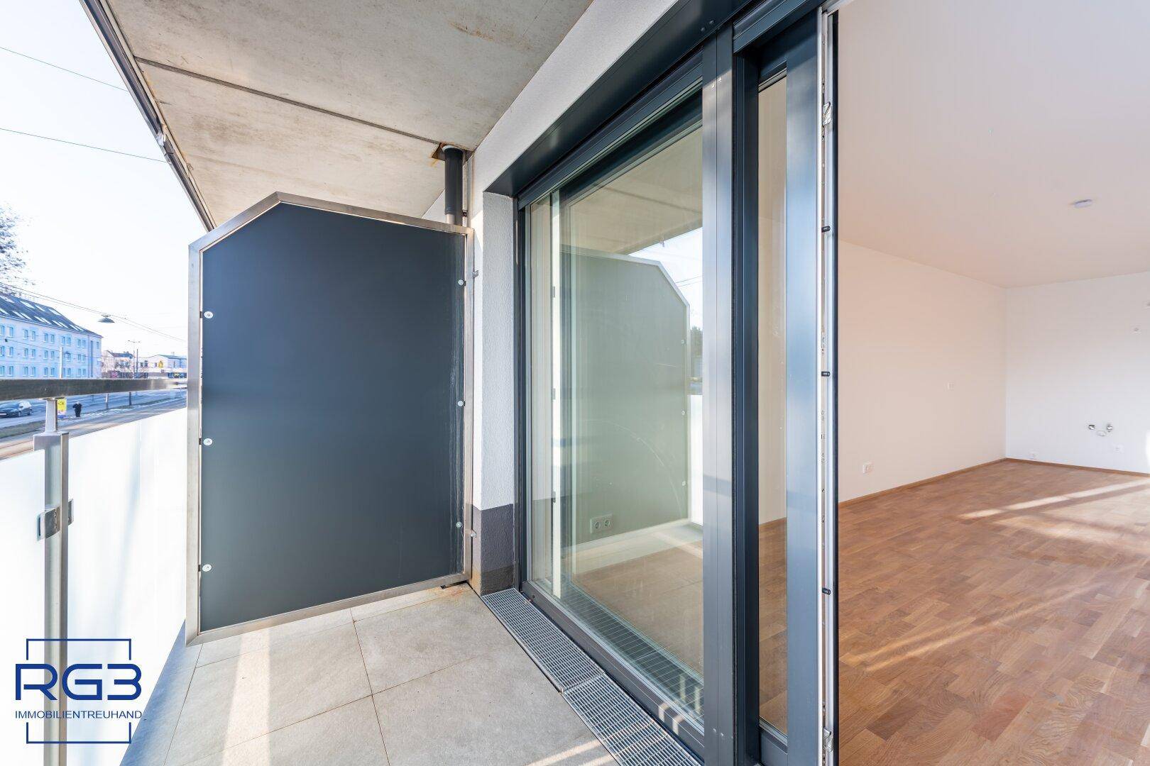 Moderner Balkon mit Schiebetür und Glasbrüstung, der einen Blick auf die Umgebung bietet.