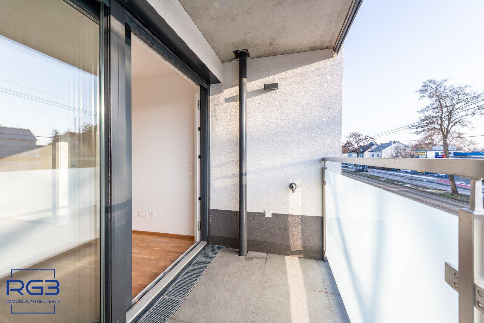Heller Balkon mit Glasgeländer und Blick auf die Straße, zugänglich vom Innenraum.