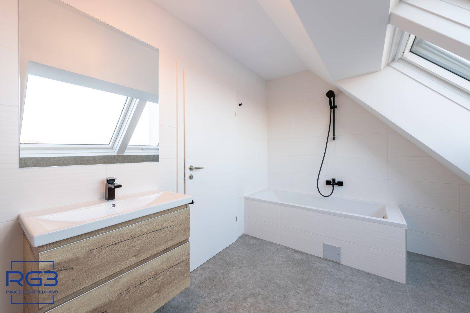 Zeitgemäßes Badezimmer mit Badewanne, Einzelwaschbecken und Dachfenster für Tageslicht.