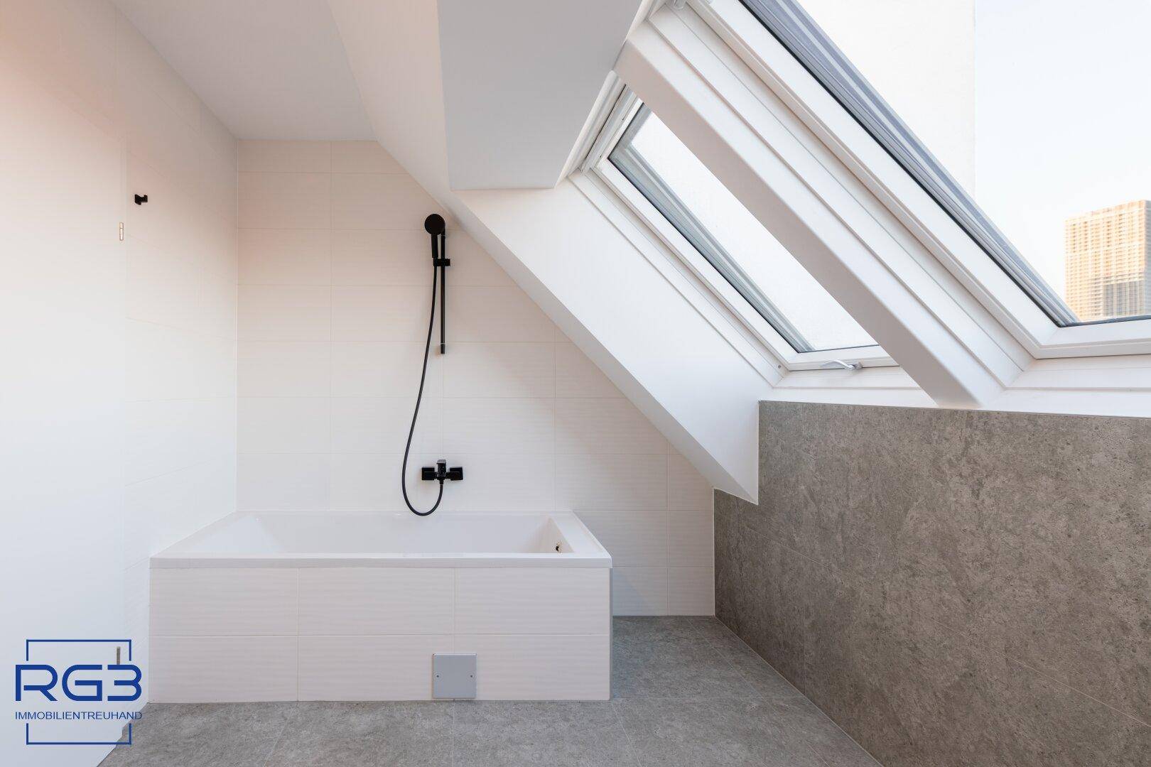 Helles Badezimmer mit Badewanne, modernen Fliesen und großen Dachfenstern.