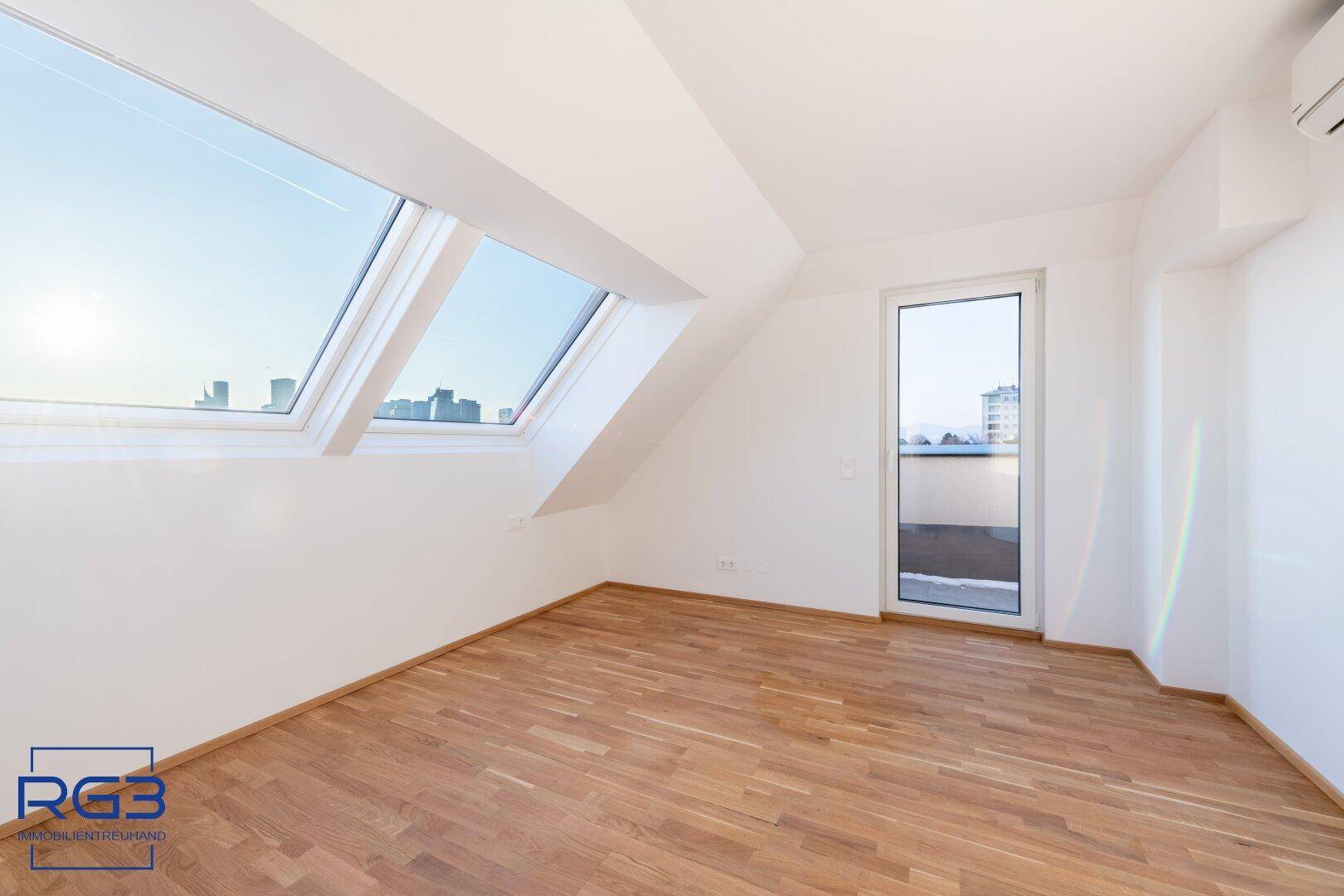 Helles Schlafzimmer mit Parkettboden, großen Dachfenstern und Zugang zur Terrasse.