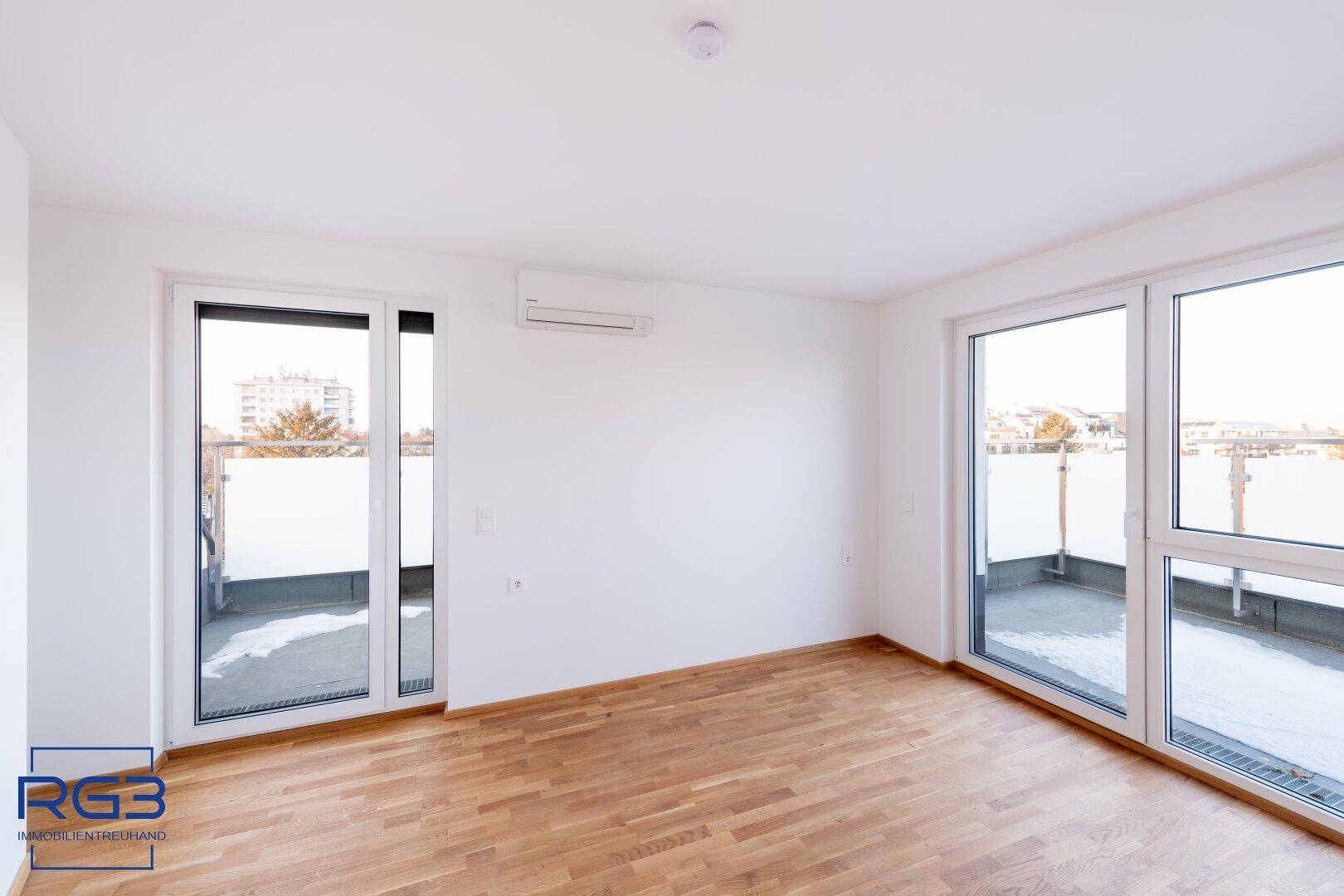 Geräumiger Wohnbereich mit vielen Fenstern, Parkettboden und Zugang zur Terrasse.