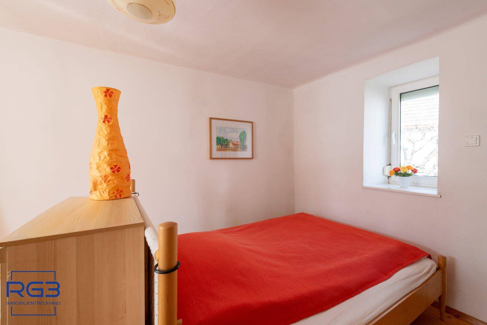 Gemütliches Schlafzimmer mit Einzelbett, Holzboden und einem Fenster mit Blick ins Grüne.