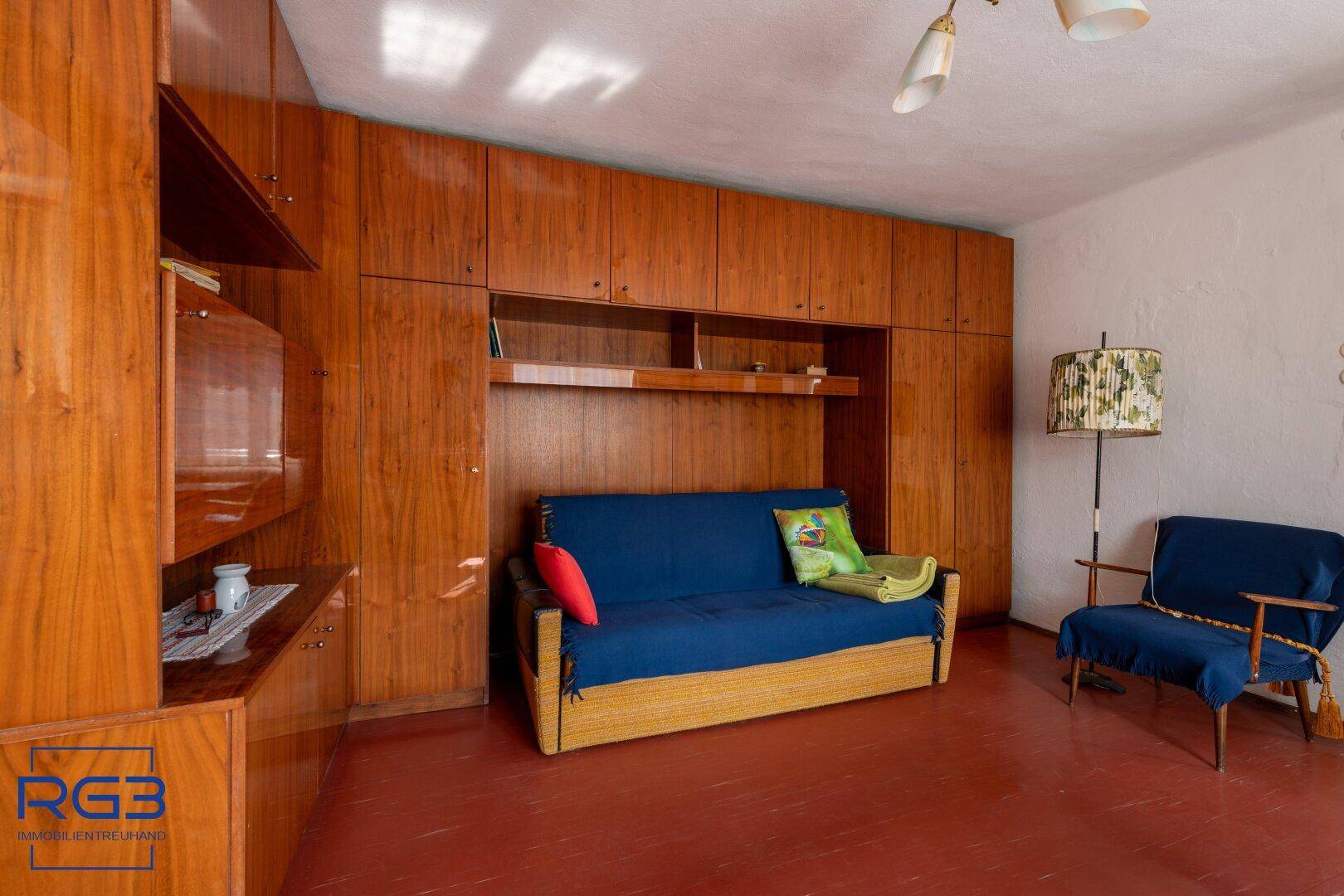 Wohnzimmer mit blauer Schlafcouch, Holzschrankwand und Stehlampe in warmen Farbtönen.