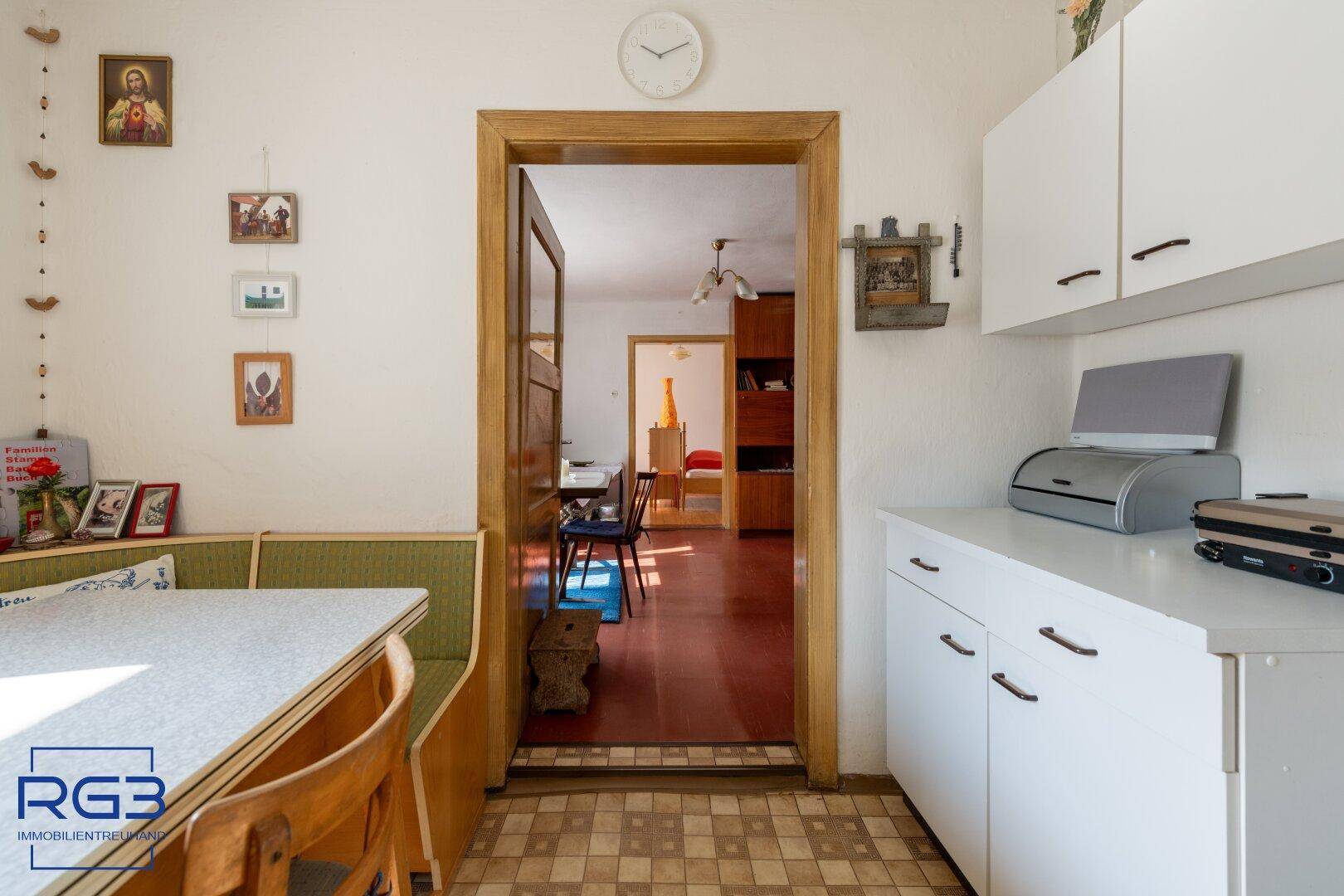 Kleine Küche mit weißen Oberschränken und Durchgang zu einem Essbereich mit Holzboden.