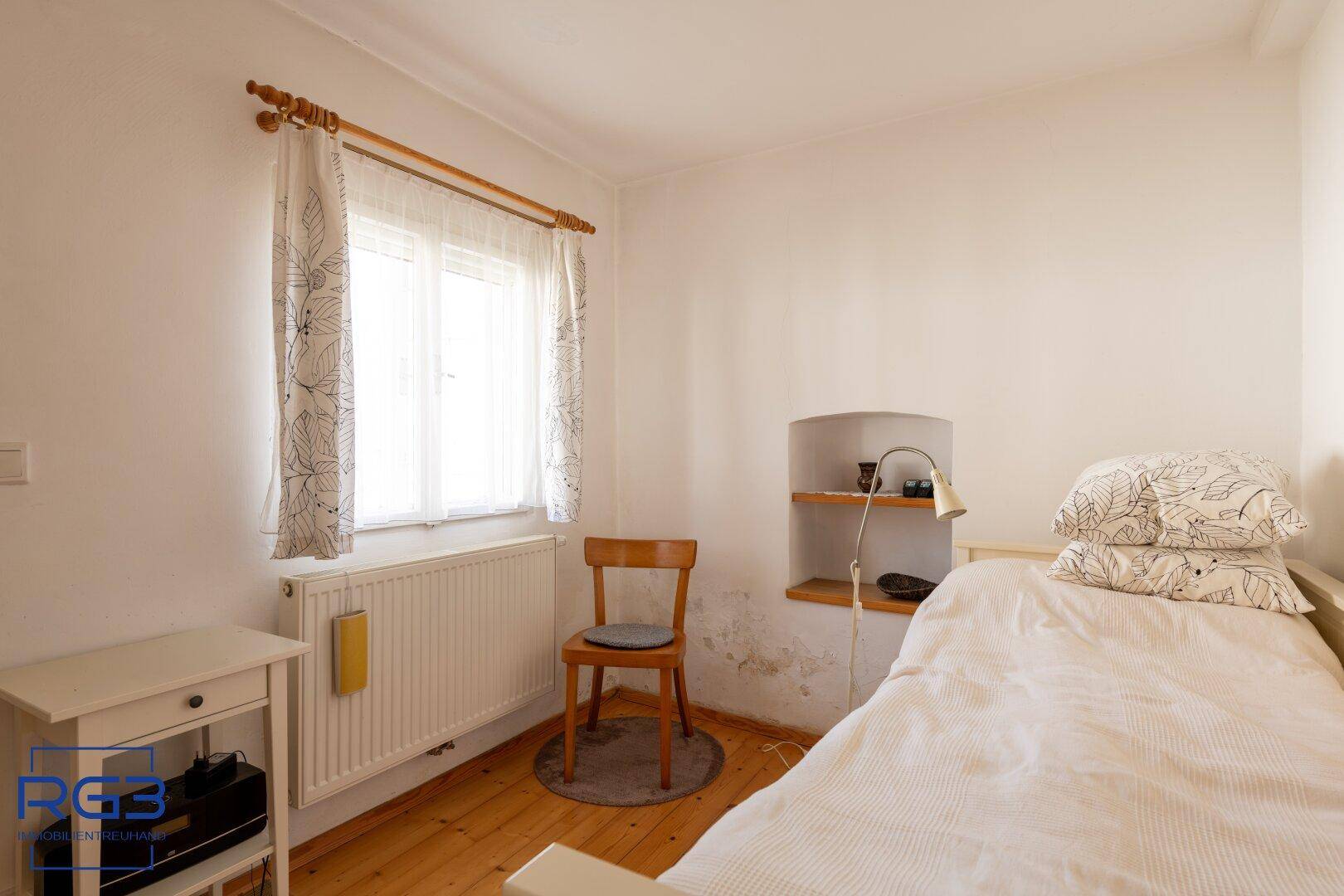 Helles Schlafzimmer mit Einzelbett, Holzboden und Fenster mit Blick ins Freie.
