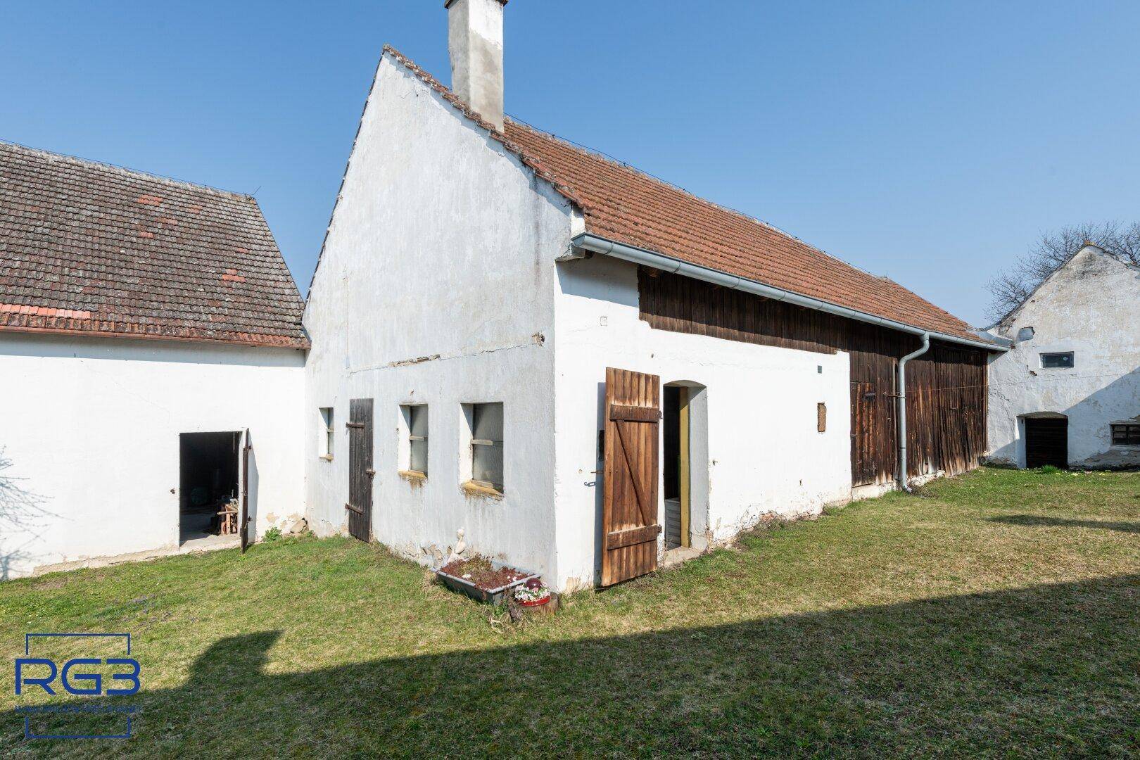Historisches Bauernhaus mit weißer Fassade, Holztüren und Ziegeldach in ländlicher Umgebung.