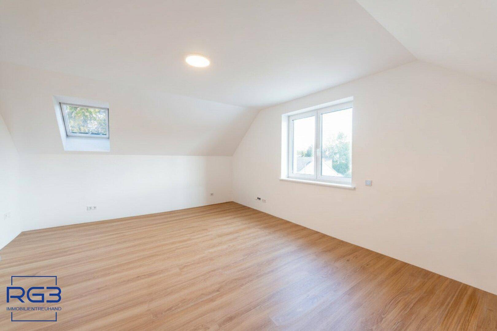 Helles Schlafzimmer im Dachgeschoss mit Laminatboden, Dachfenster und zusätzlichem Fenster.