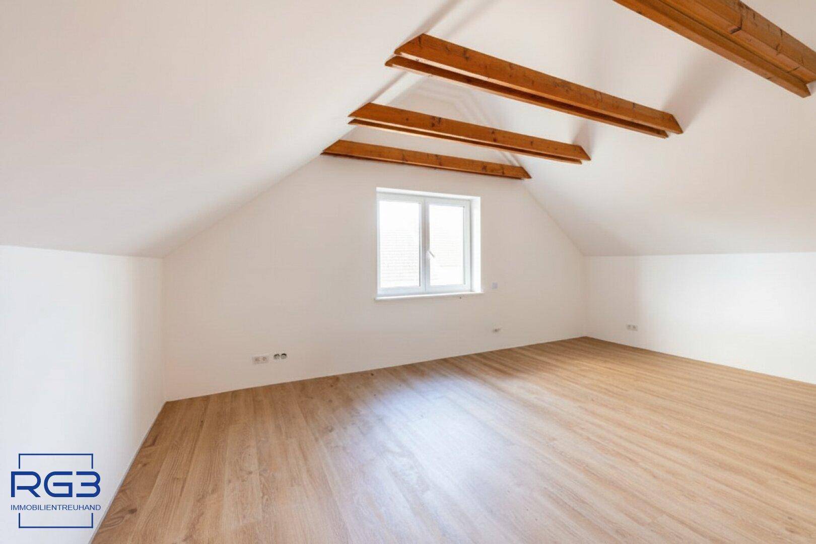 Geräumiges Schlafzimmer im Dachgeschoss mit Holzbalken, Fenster und Laminatboden.