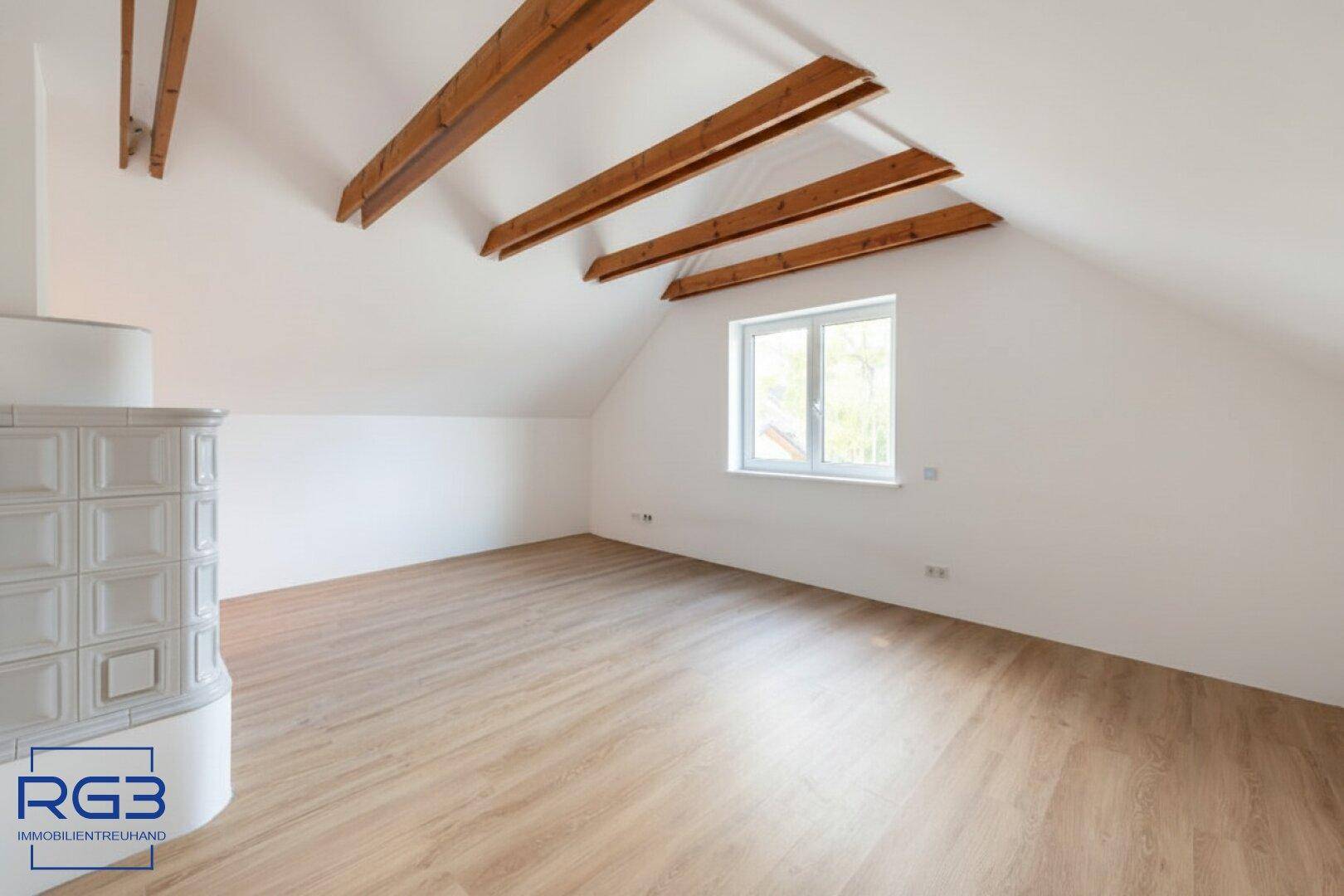 Helles Dachgeschosszimmer mit Holzbalken, Fenster und Laminatboden, ideal als Büro oder Schlafzimmer.