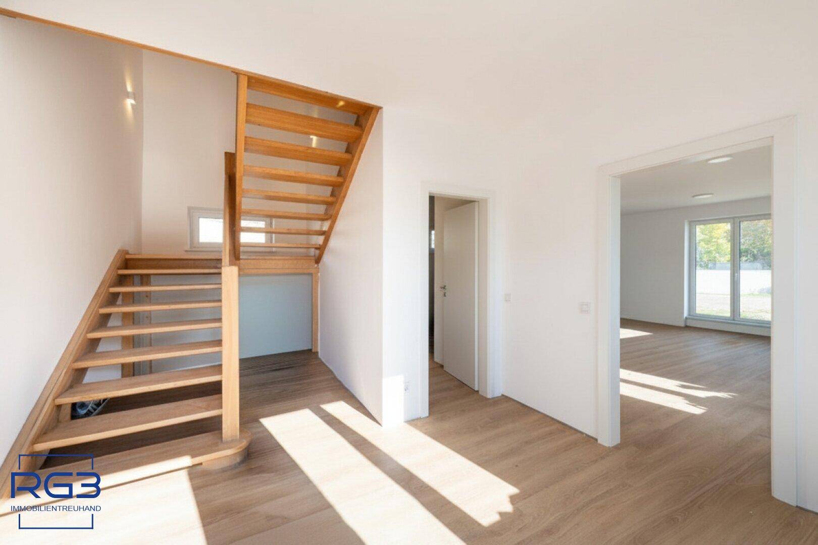 Heller Eingangsbereich mit Holztreppe und Laminatboden, führt zu weiteren Räumen.