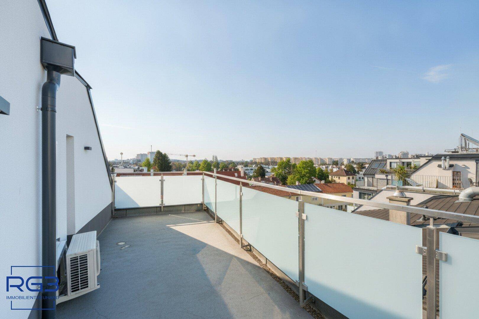 Weitläufige Terrasse mit Glasgeländer und freiem Blick auf die Stadt und den Himmel.