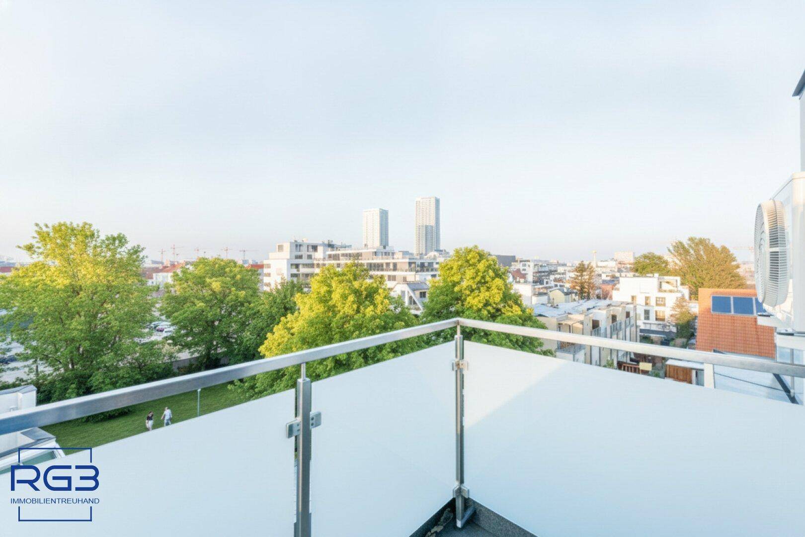Terrasse mit Glasgeländer und Blick auf grüne Bäume und die städtische Skyline.