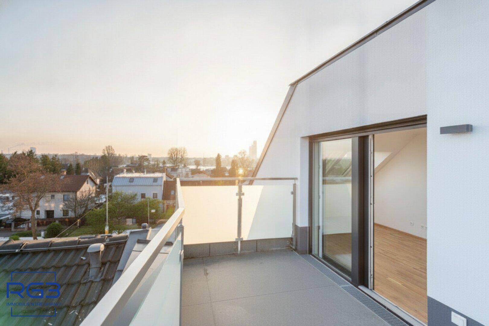 Terrasse mit Glasgeländer und weitem Blick über die Dächer der Stadt bei Sonnenuntergang.