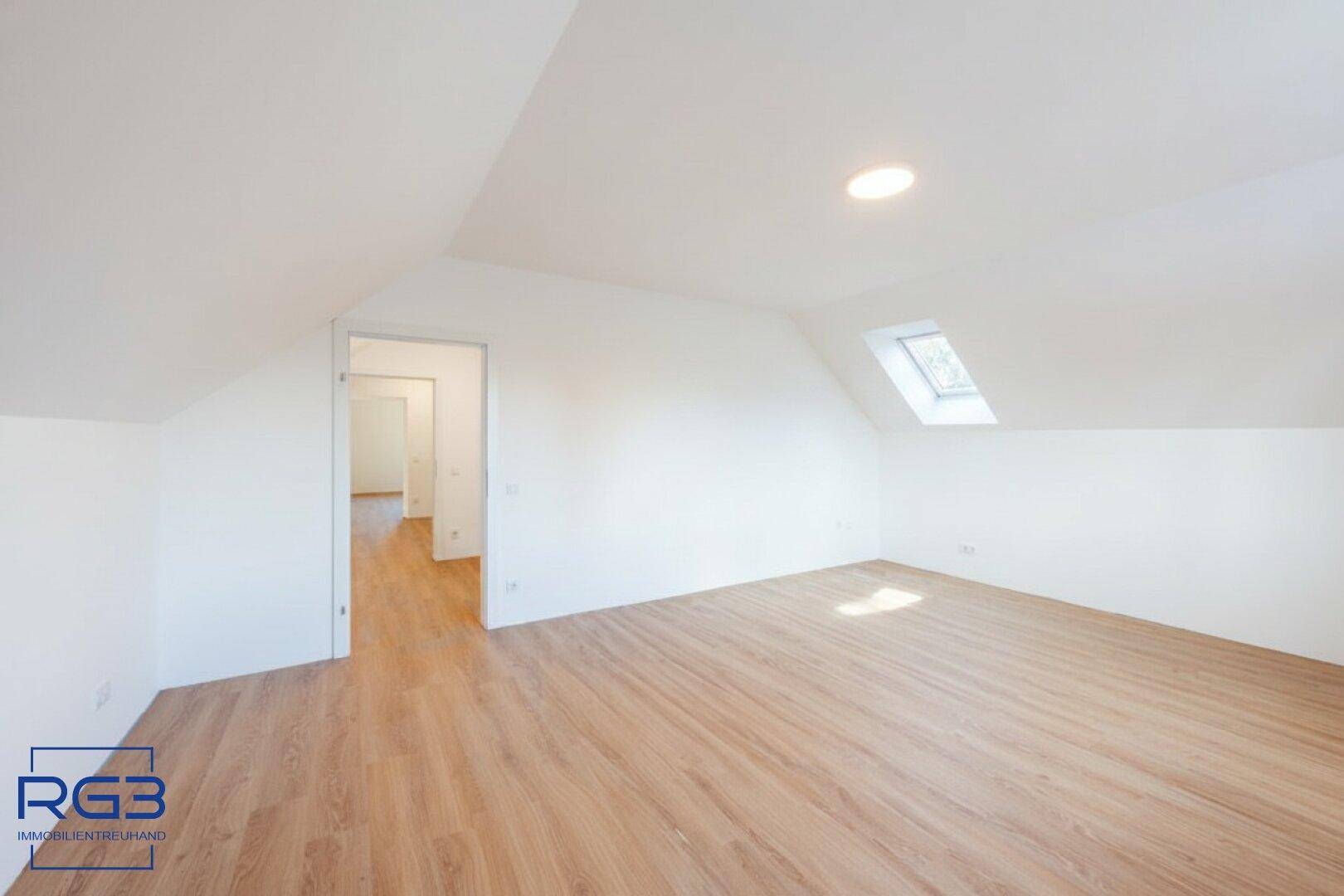 Geräumiges Schlafzimmer im Dachgeschoss mit Laminatboden, Dachfenster und Zugang zum Flur.