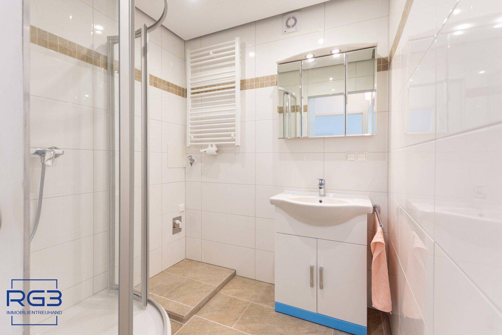 Modernes Badezimmer mit weiß gefliesten Wänden, Duschkabine und Waschtisch mit Spiegelschrank.