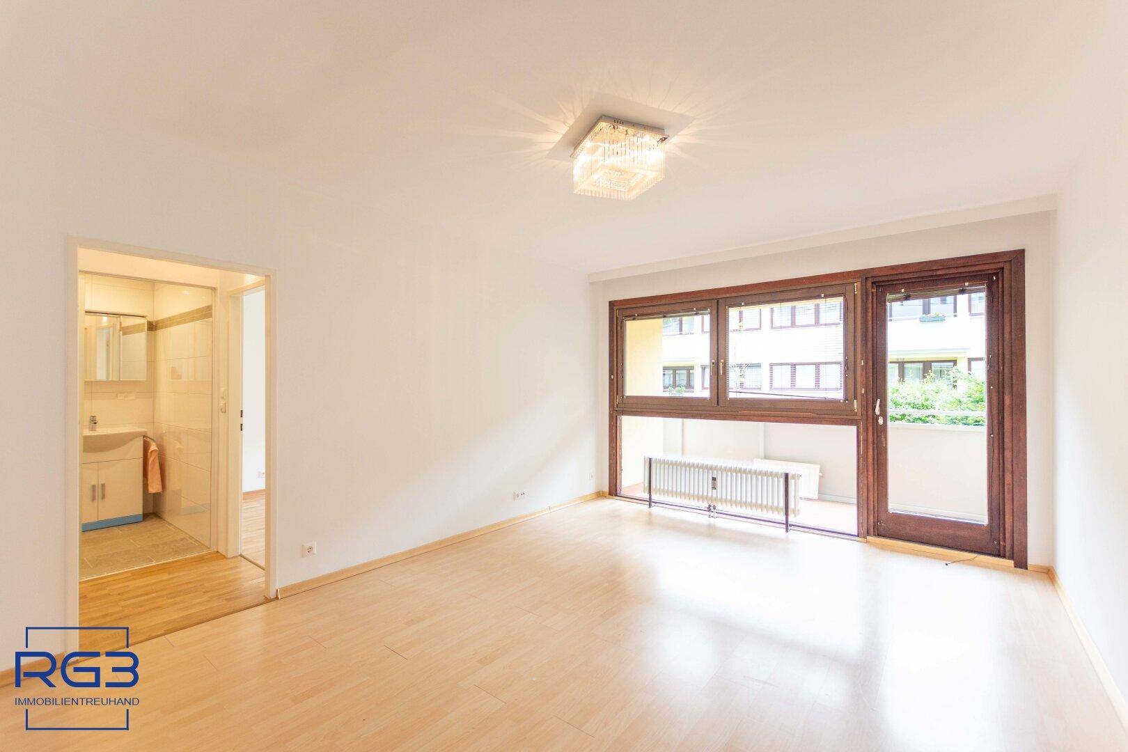 Geräumiges Wohnzimmer mit hellem Parkettboden, weiß gestrichenen Wänden und Zugang zum Balkon.