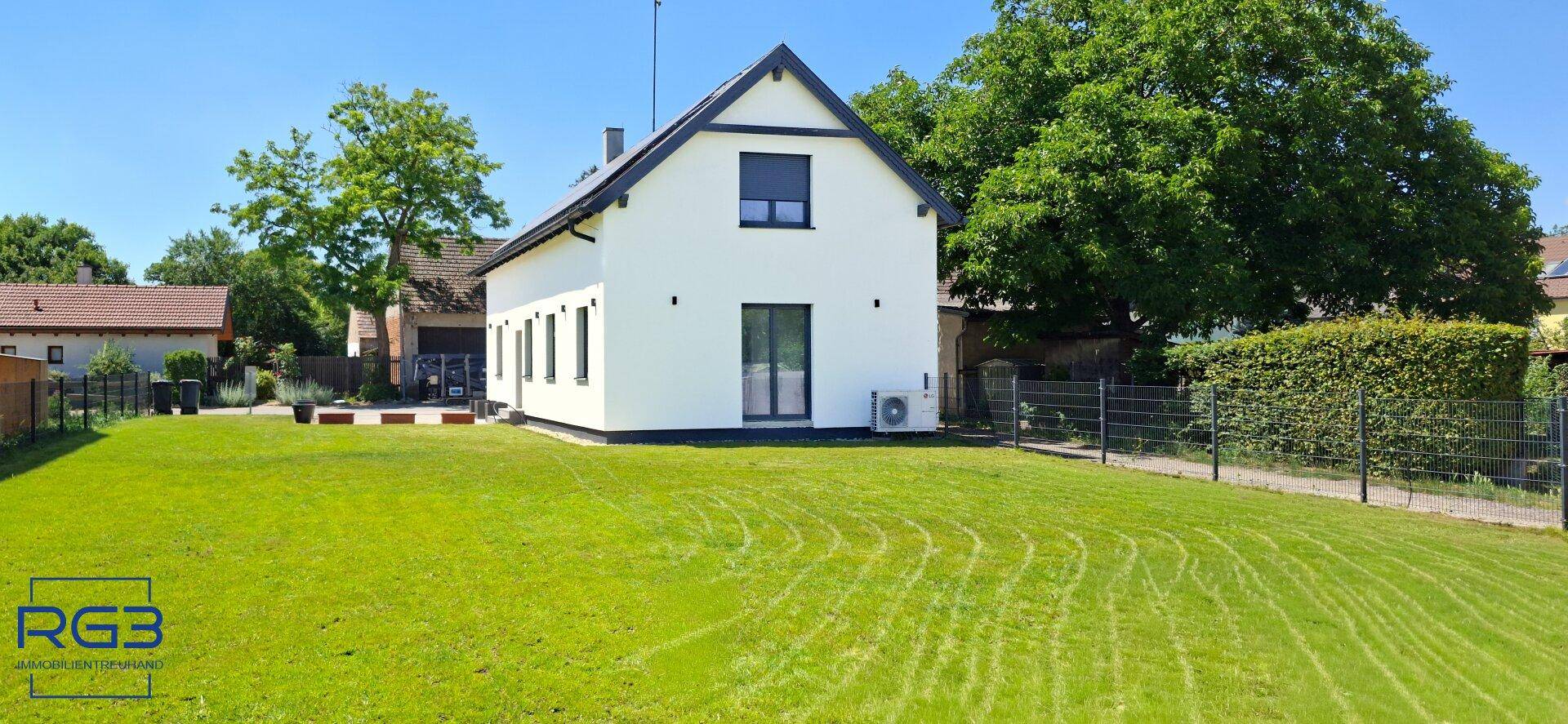 Modernes Einfamilienhaus mit weißer Fassade, großem Rasen und blauer Himmel.