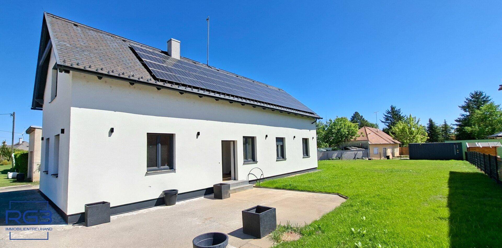 Seitenansicht des Hauses mit gepflasterter Terrasse und großem Gartenbereich.
