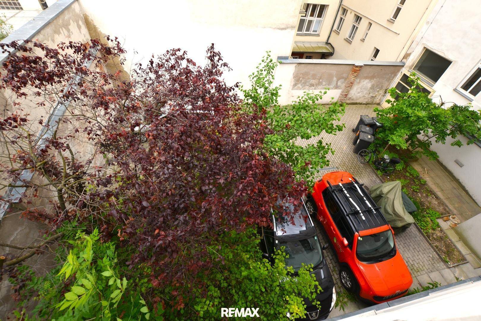 Blick von oben auf einen begrünten Innenhof mit parkenden Autos.