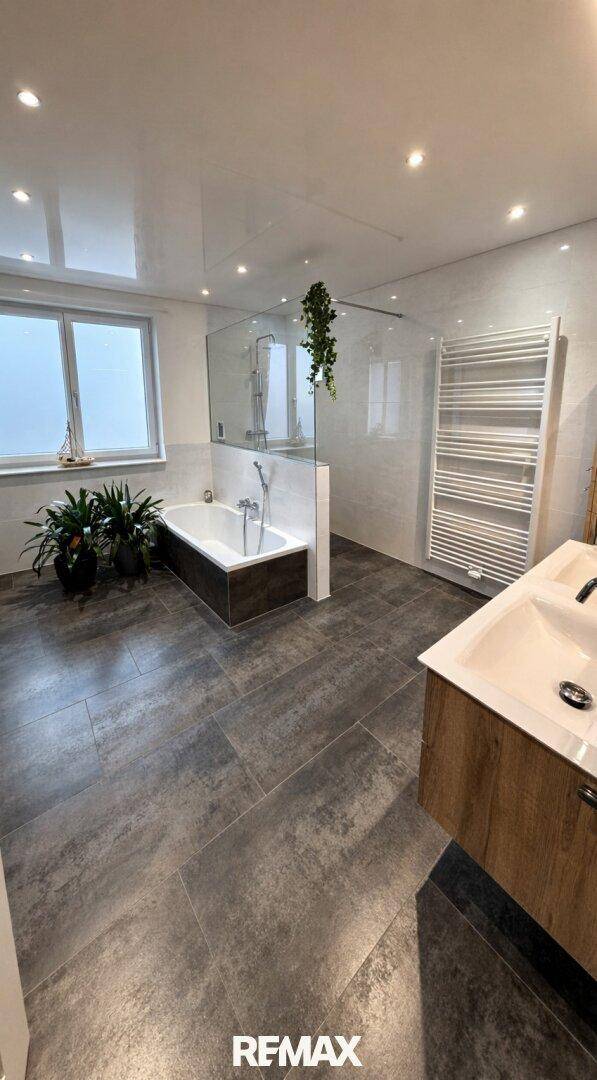 Modernes Badezimmer mit Badewanne, begehbarer Dusche, Doppelwaschbecken und großformatigen Fliesen.