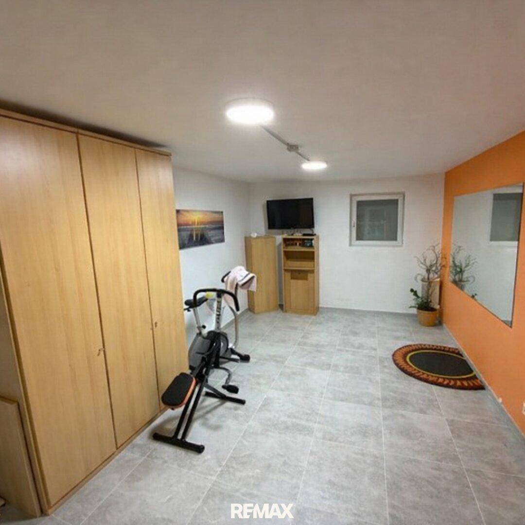 Vielseitiger Fitnessraum im Untergeschoss mit Trainingsgeräten, Spiegelfläche und Fliesenboden.
